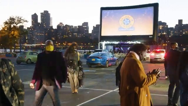 Radial Park drive-in theater at dusk — a giant screen against the Manhattan skyline as guests arrive