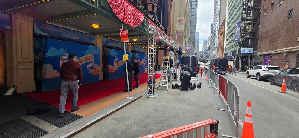Crew rigging truss and lighting over a red carpet ahead of doors
